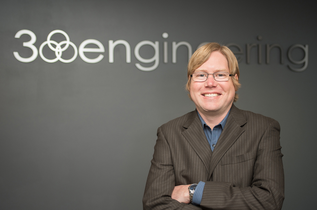 About a person with glasses, wearing a suit, standing confidently with arms crossed in front of a wall where the word "engineering" is partially visible, capturing the essence of professionalism and innovation.